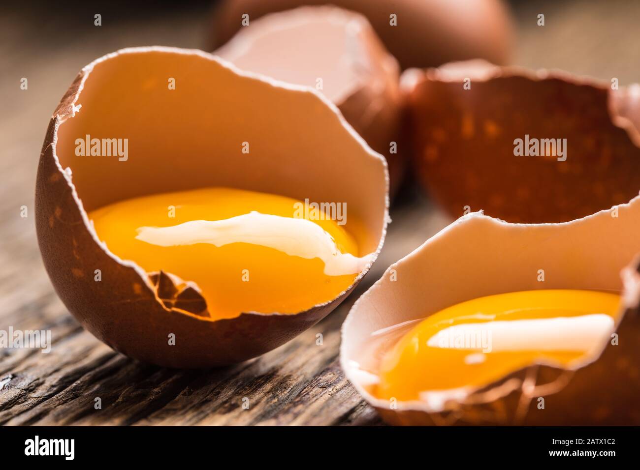 Broken chicken eggs with yolk on wooden table Stock Photo
