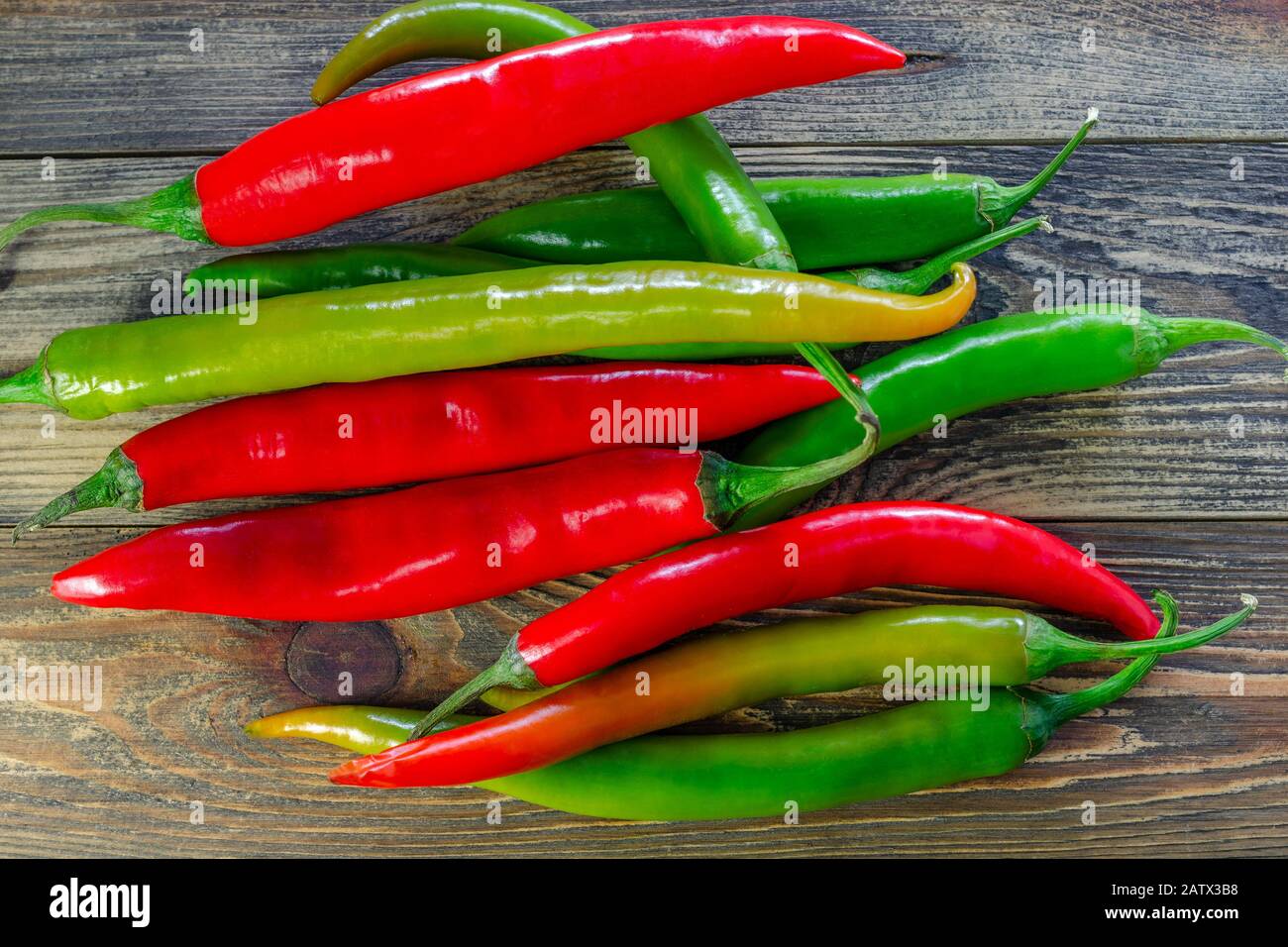 Mix of heap of raw red and green chili pappers or Capsicum frutescens,  on dark wooden table. Food background. Top view. Selective focus. Close-up. Stock Photo