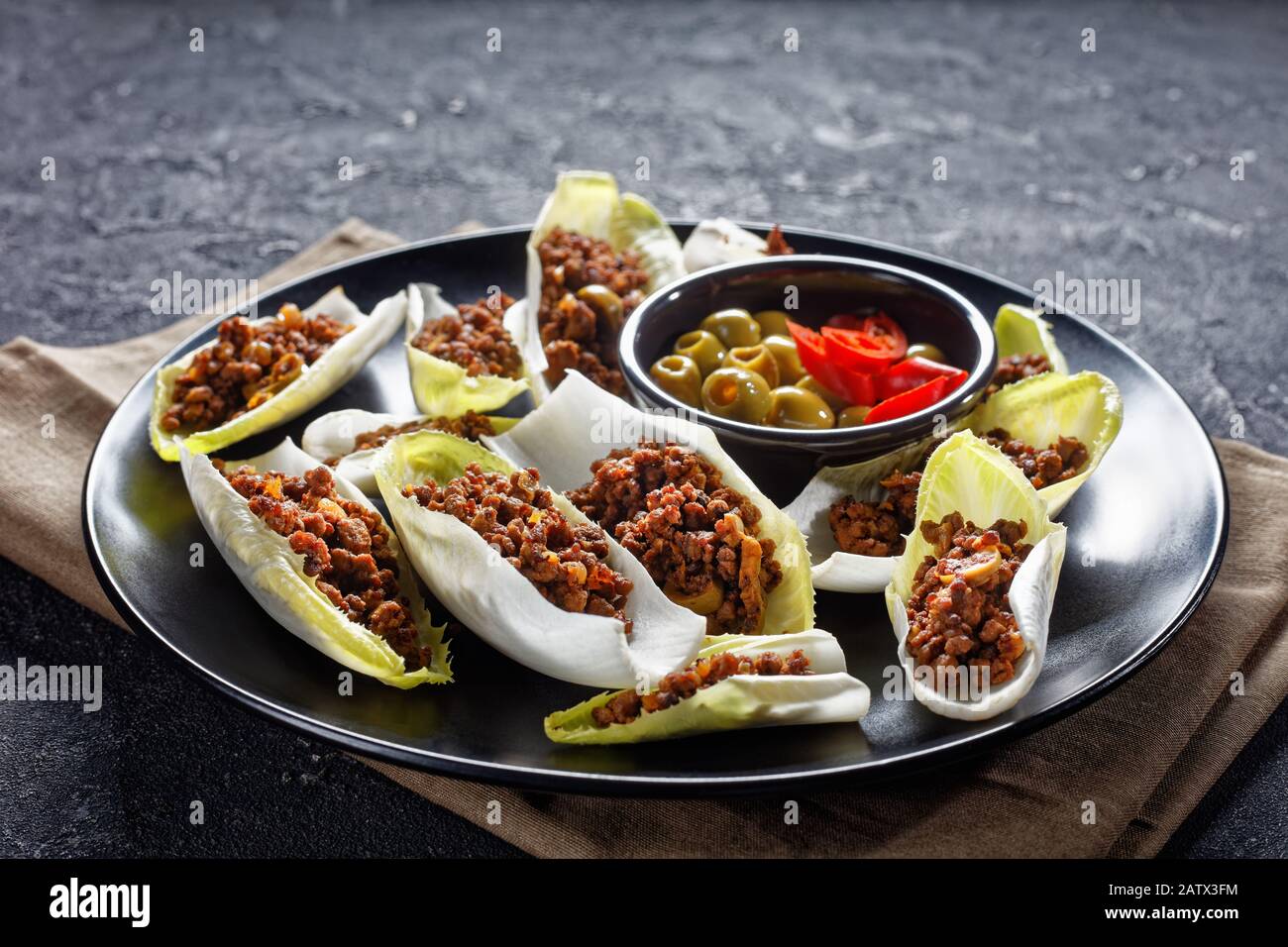 low-carb Ground Beef and chopped green olives Endive Boats served on a black plate on a grey concrete table, horizontal view from above Stock Photo