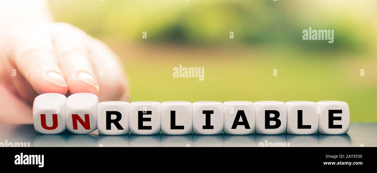 Hand turns dice and changes the word 'unreliable' to 'reliable'. Stock Photo