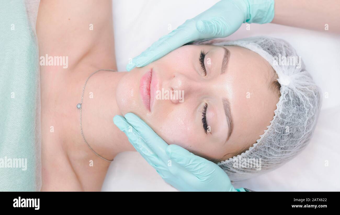 The female dermatologist do face massaged to beautiful girl cosmetology cabinet or beauty clinic. Concept of face cleanser, skin and health care Stock Photo