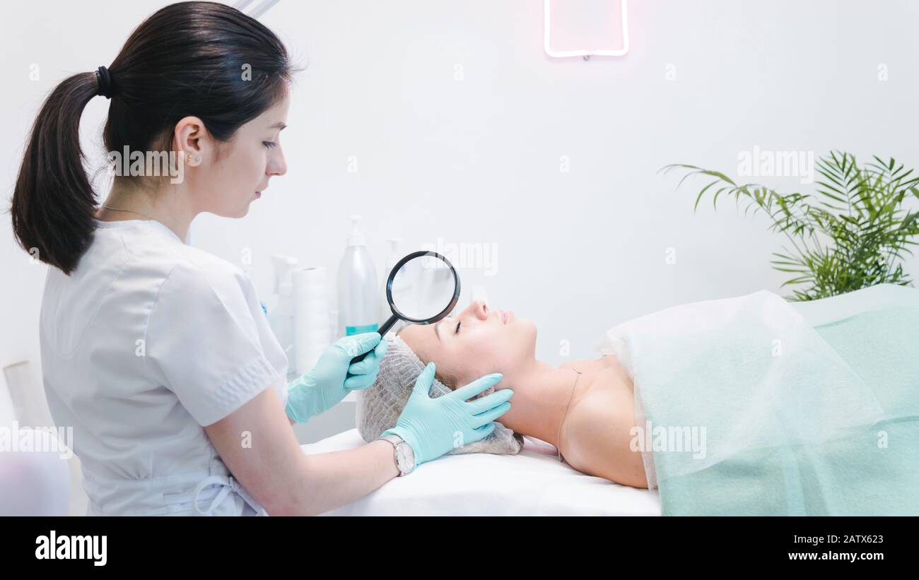 The female dermatologist examining face of young patient with