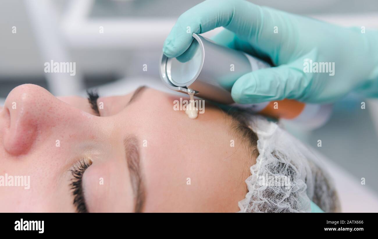 The female dermatologist do face massaged to beautiful girl cosmetology cabinet or beauty clinic. Concept of face cleanser, skin and health care Stock Photo