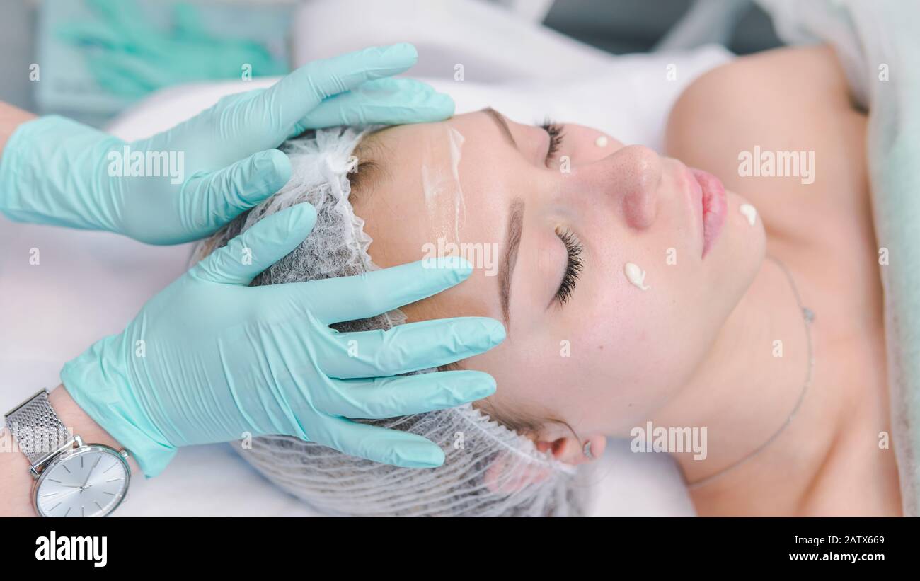 The female dermatologist do face massaged to beautiful girl cosmetology cabinet or beauty clinic. Concept of face cleanser, skin and health care Stock Photo