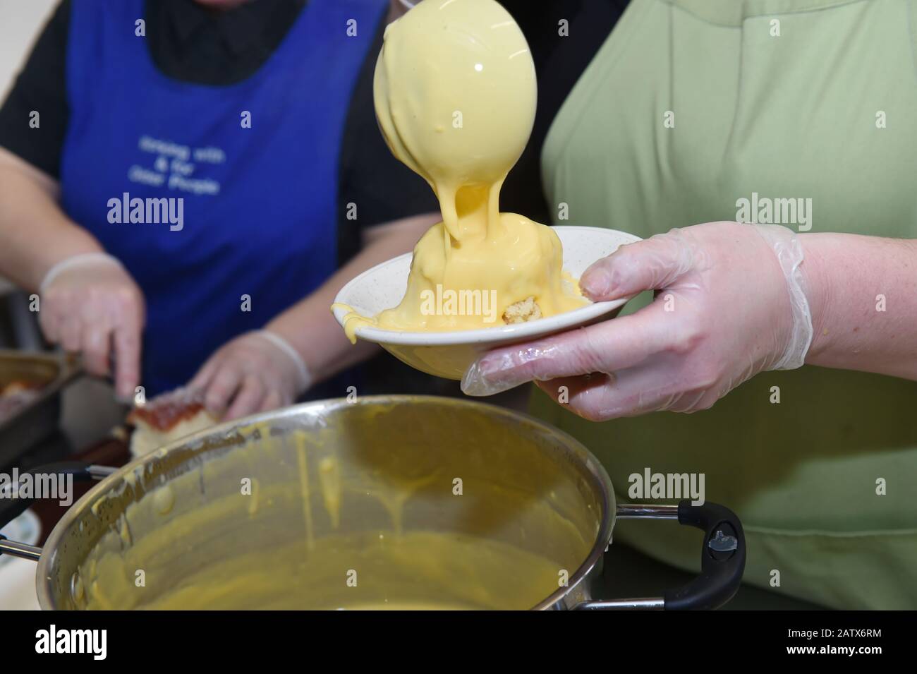 Custard is poured onto a hot pudding in a drop in centre for older people, Leeds UK Stock Photo