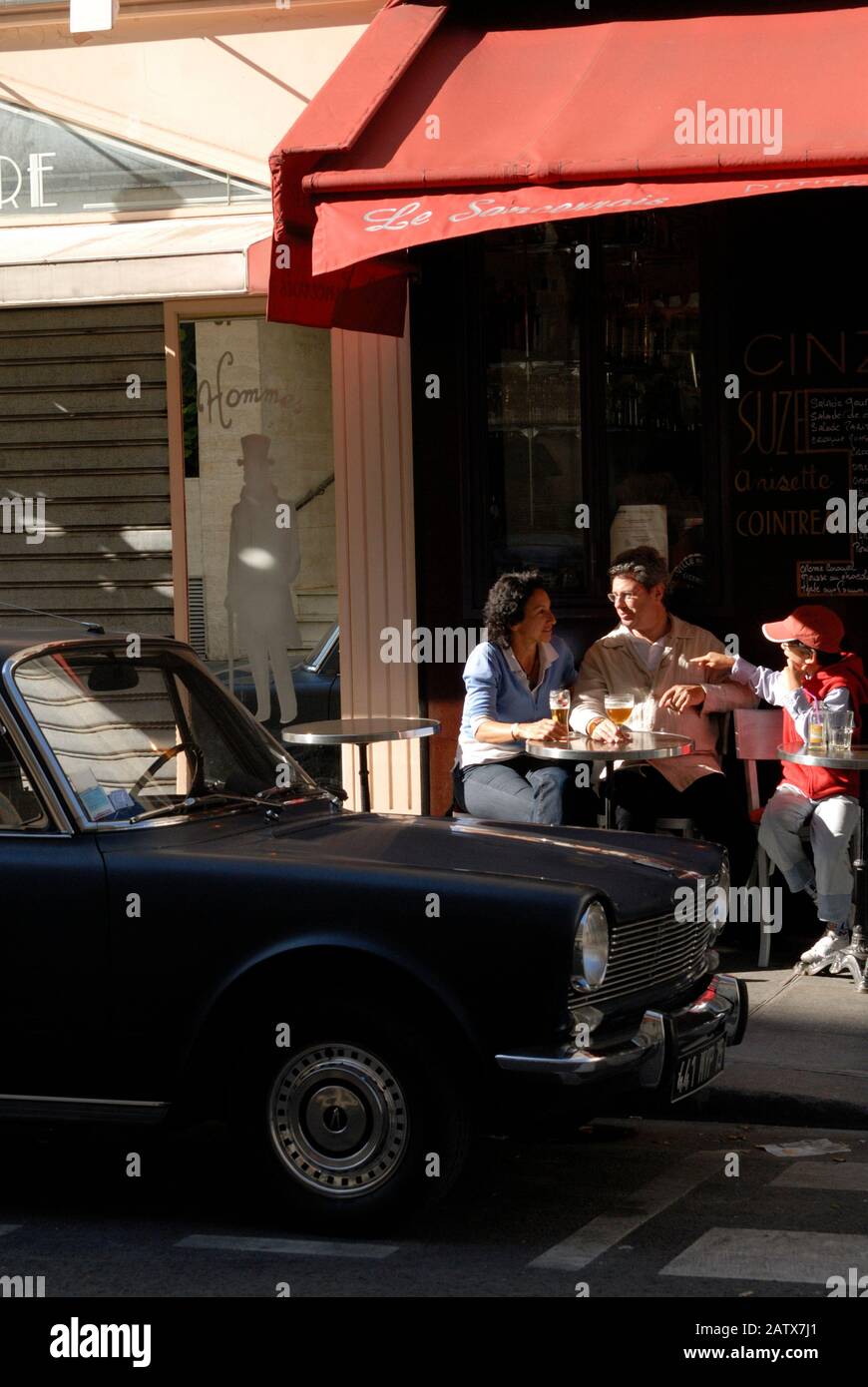 PARIS CAR AND CAFÉ TERRASSE - FAMILY HAVING A DRINK IN A SMALL PARIS CAFÉ WITH A SIMCA 1000 PARKED IN FRONT - STREET CAR PHOTOGRAPHY © F.BEAUMONT Stock Photo
