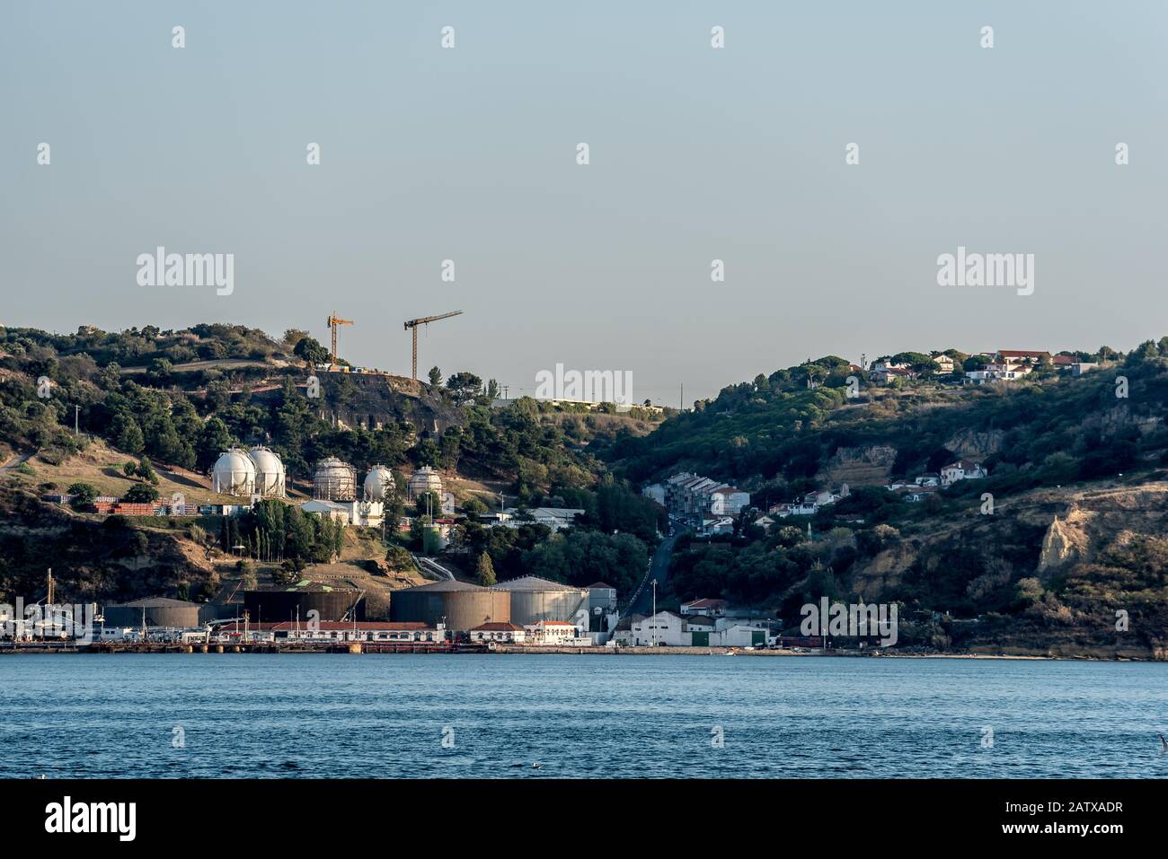 Industrial silos tanks and storage at shipping terminal next to urban area on the Tejo River in Portugal in afternoon sunshine Stock Photo