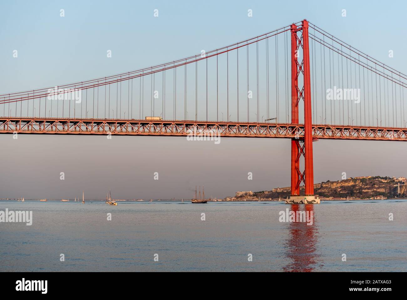 Tower and span of 25 de Abril bridge in Lisbon Portugal in afternoon sunshine and calm sea with pleasure boats underneath Stock Photo