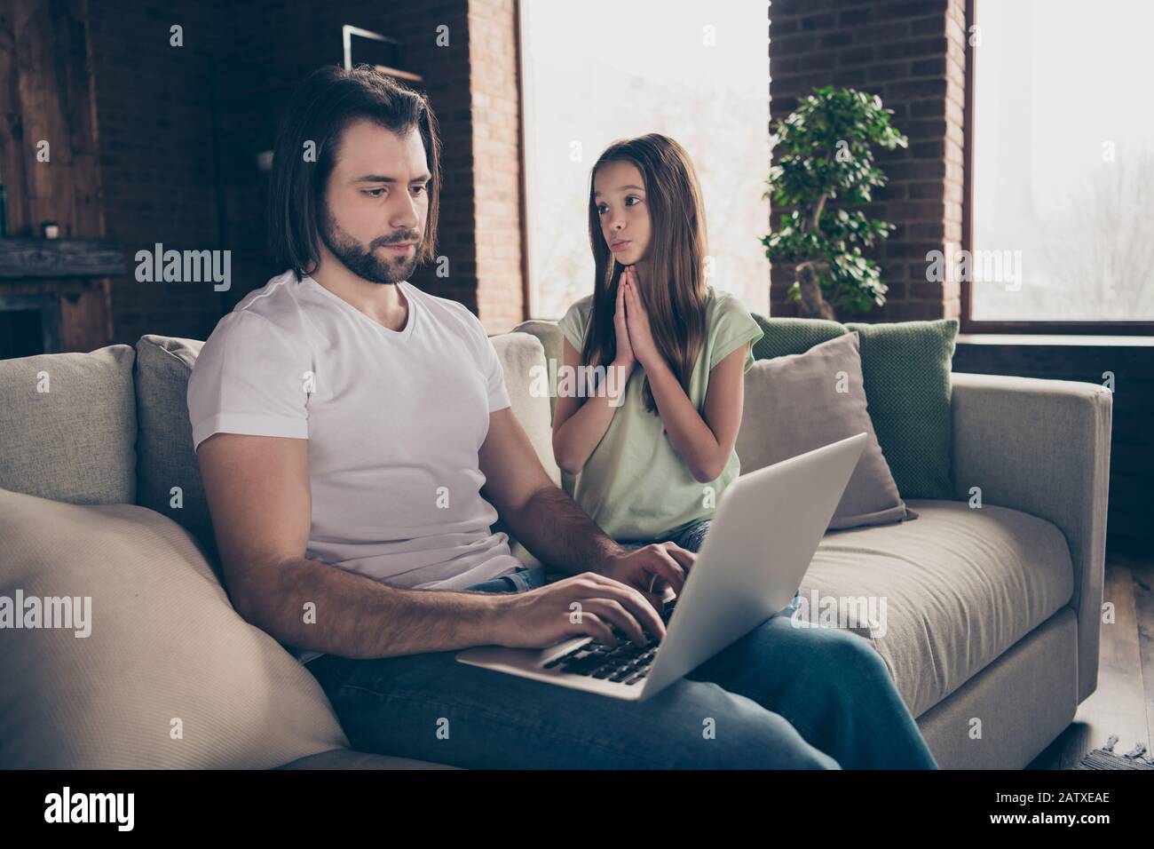 Photo of little pretty funny expression lady holding hands together begging  handsome dad give her notebook want to watch movie sitting sofa house room  Stock Photo - Alamy