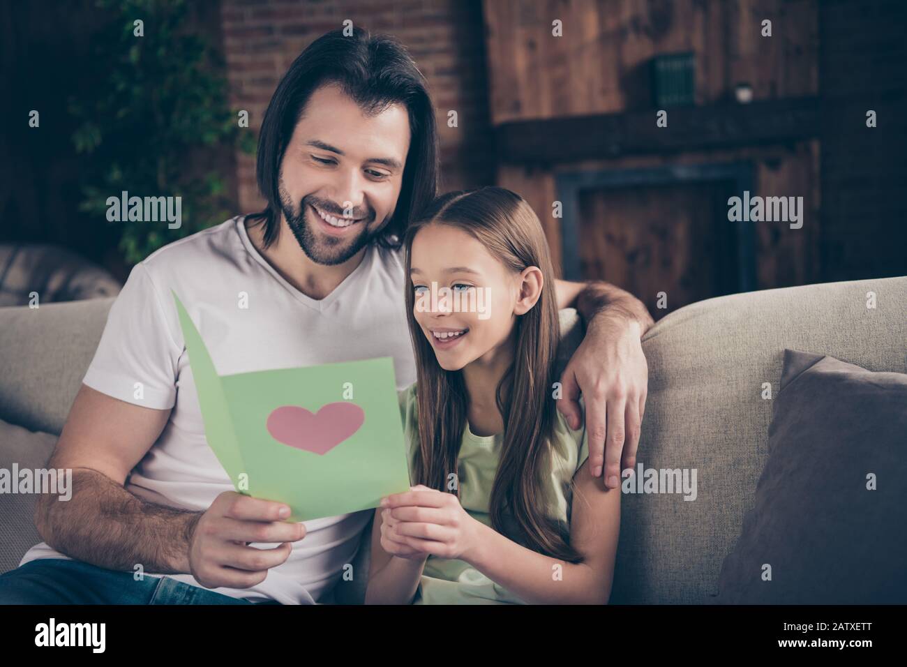 Photo of little adorable funny lady her handsome daddy sit cozy sofa hugging hold cute card birthday present reading greeting celebrate best day Stock Photo