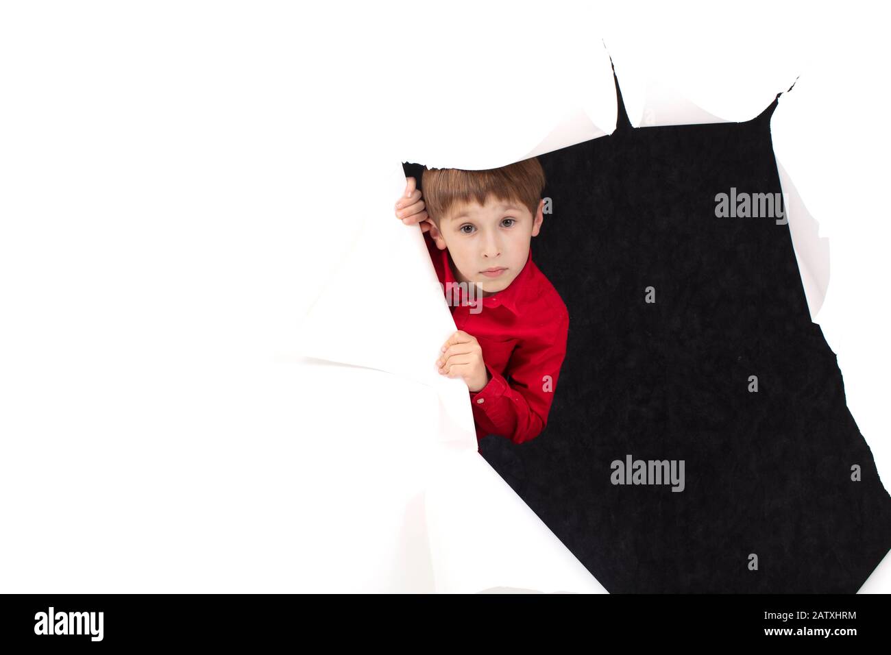 A child from a hole in paper. Boy shows cardboard. Look out of the billboard. The concept of surprise and novelty.A curious face looks in surprise fro Stock Photo