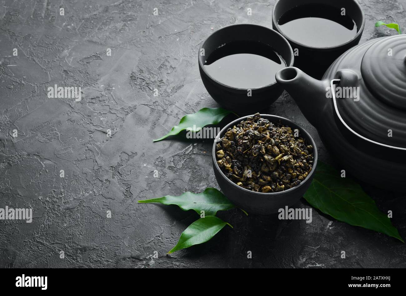 Chinese green tea in a cup with a kettle. On a black stone background