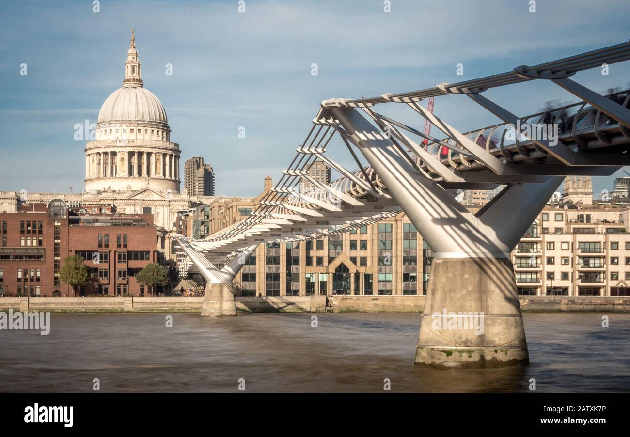 Long exposure blurring the water of the River Thames as it flows underneath the Millennium Bridge leading towards St. Paul's cathedral in the distance Stock Photo
