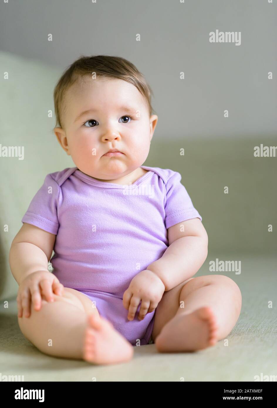 Thoughtful and serious nice baby girl sitting on the couch at home Stock Photo