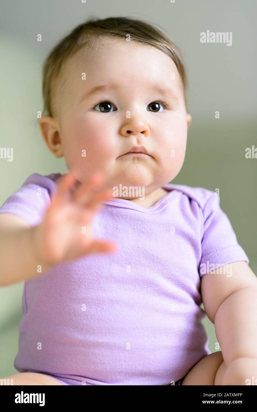 Baby girl plays raising hand at home Stock Photo