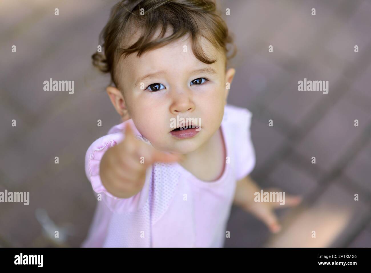 The one-year-old child looking up and points his finger at the camera. Cute baby girl is tired to play and asks for the hand. Stock Photo