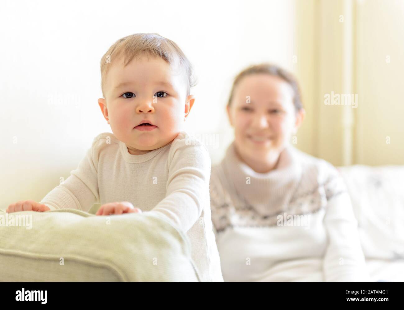 Baby girl plays with mother on the couch at home. Baby attentively looks. Stock Photo