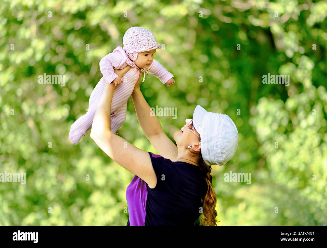 Happy mother throws up baby in nature on blurred background Stock Photo