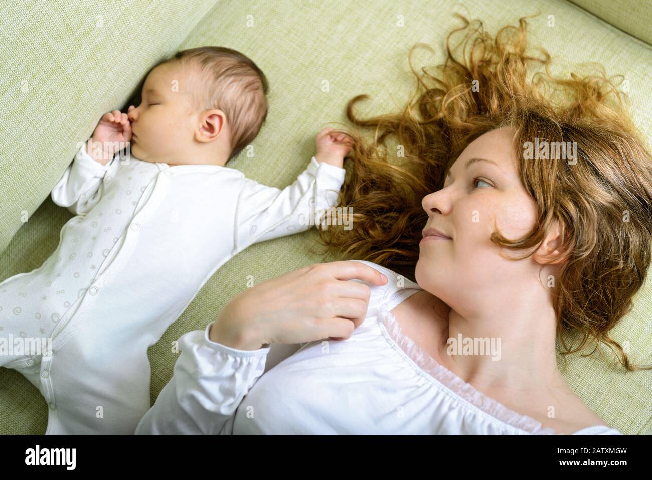 Beautiful woman looks at her newborn daughter on the couch at home Stock Photo