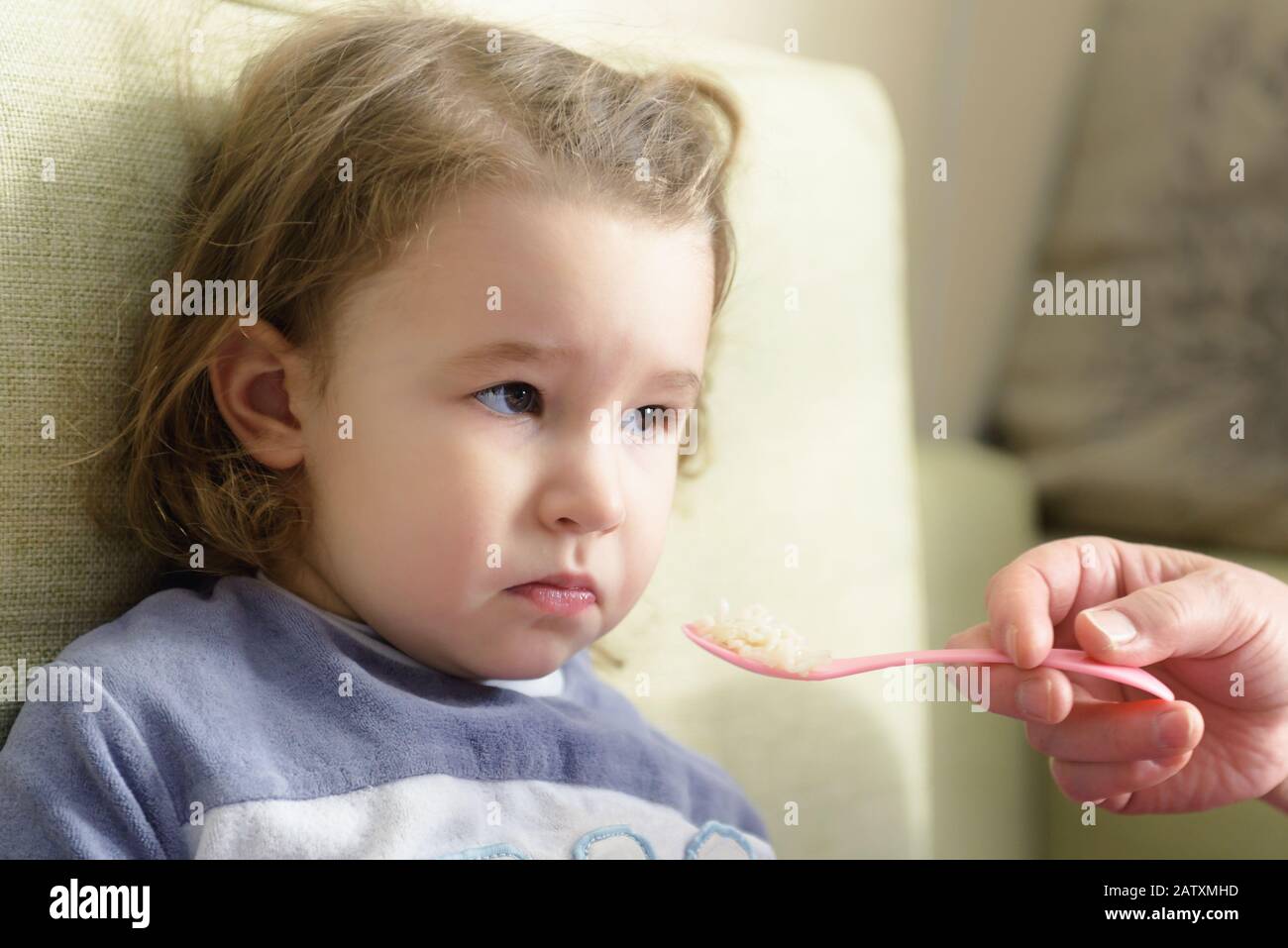 Child refuses to eat. The three year old kid is fed with a spoon at home. Cute baby girl grimaces because she does not like the food. Portrait of funn Stock Photo