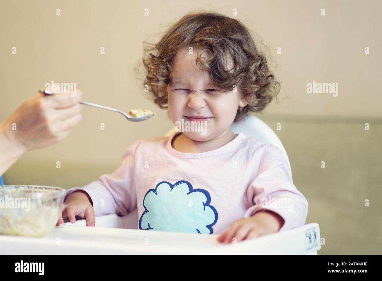 Mother feeds the baby with a spoon. The two-year child is naughty and refuses to eat. Stock Photo