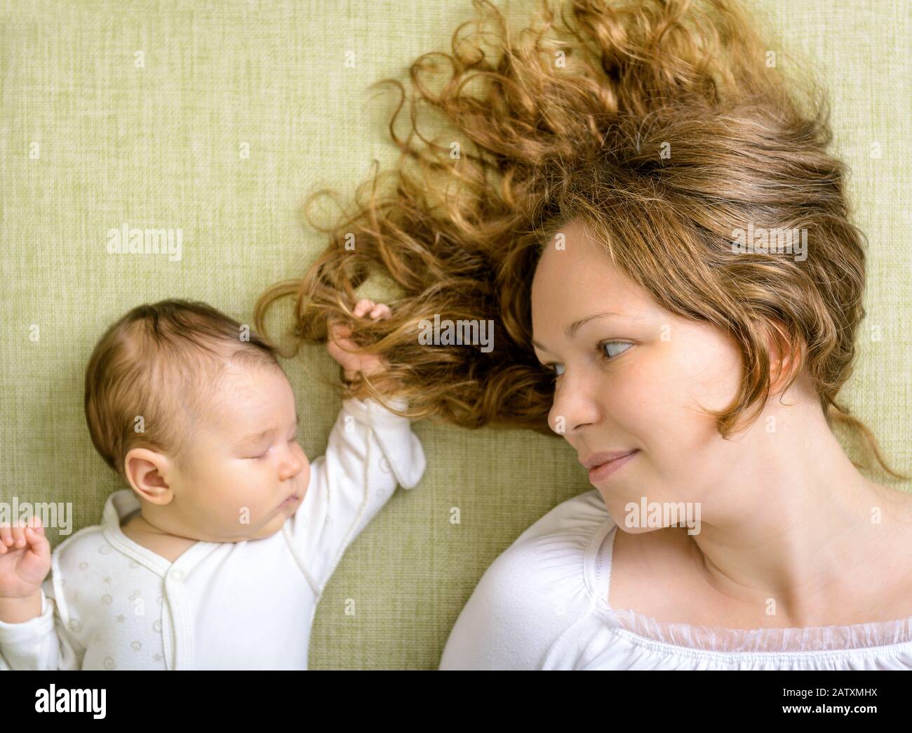 Beautiful woman looks at her newborn daughter on the couch at home Stock Photo
