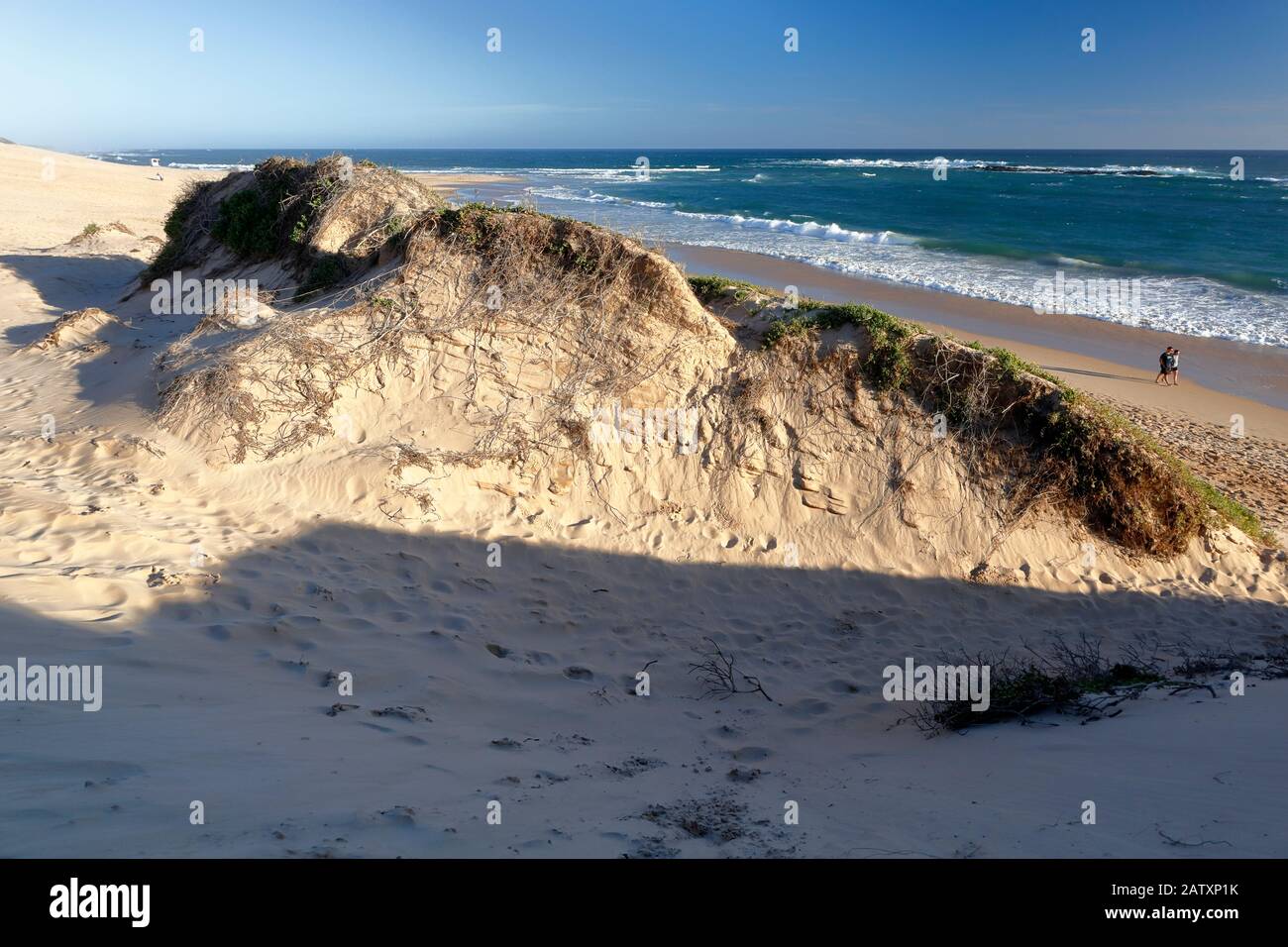 Couple walking along the beach next to the towering sand dunes of