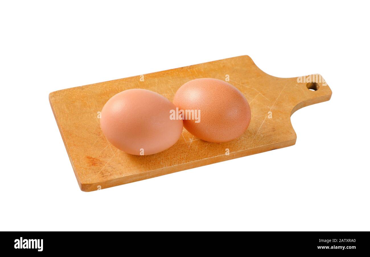 Two brown eggs on wooden cutting board isolated on white Stock Photo