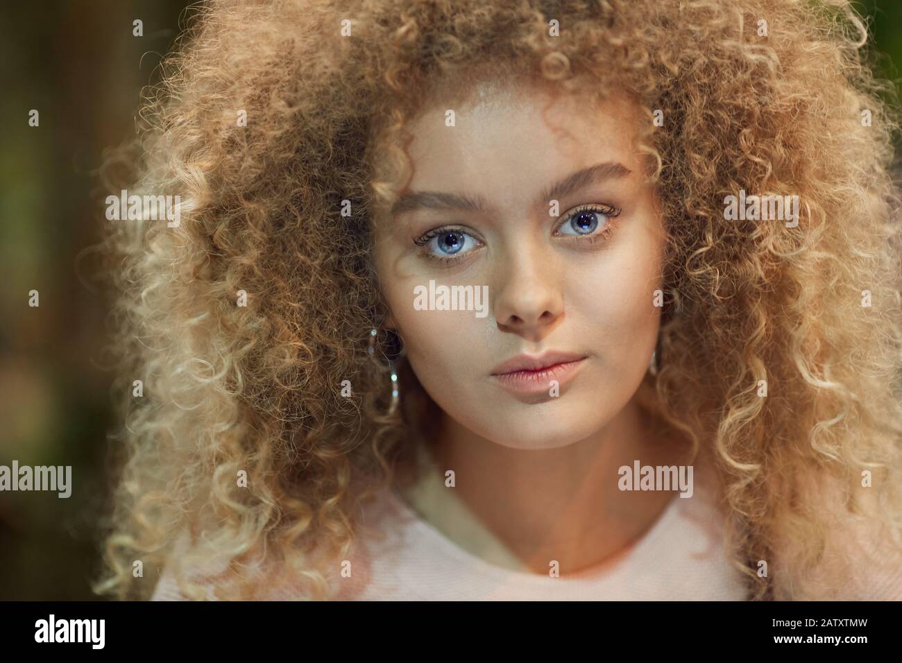 Portrait of young beautiful woman with curly blonde hair looking at camera Stock Photo