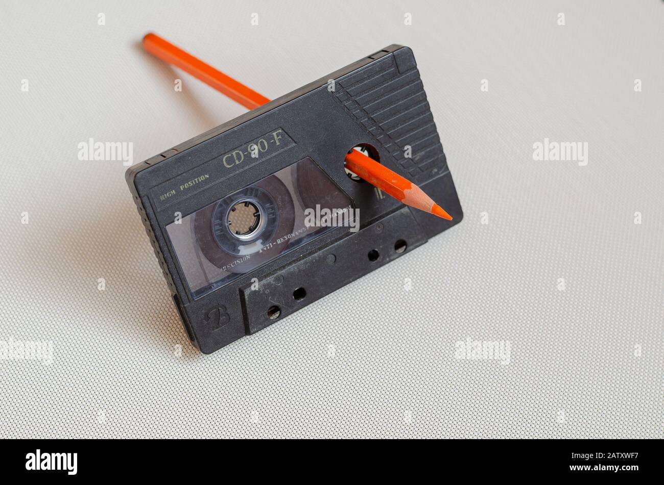 Black audio cassette and orange pencil on a light background. Manual