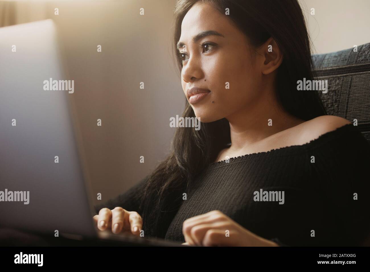 Beautiful young woman remotely working on a laptop computer at home. Stock Photo
