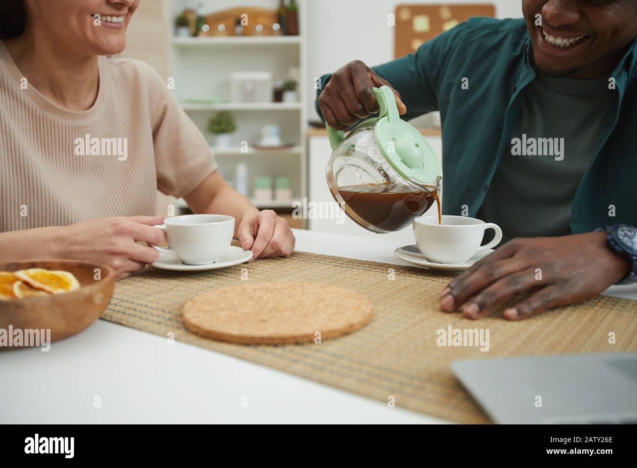 Close-up of young multiethnic couple enjoying each other and drinking coffee at the table in the domestic kitchen Stock Photo