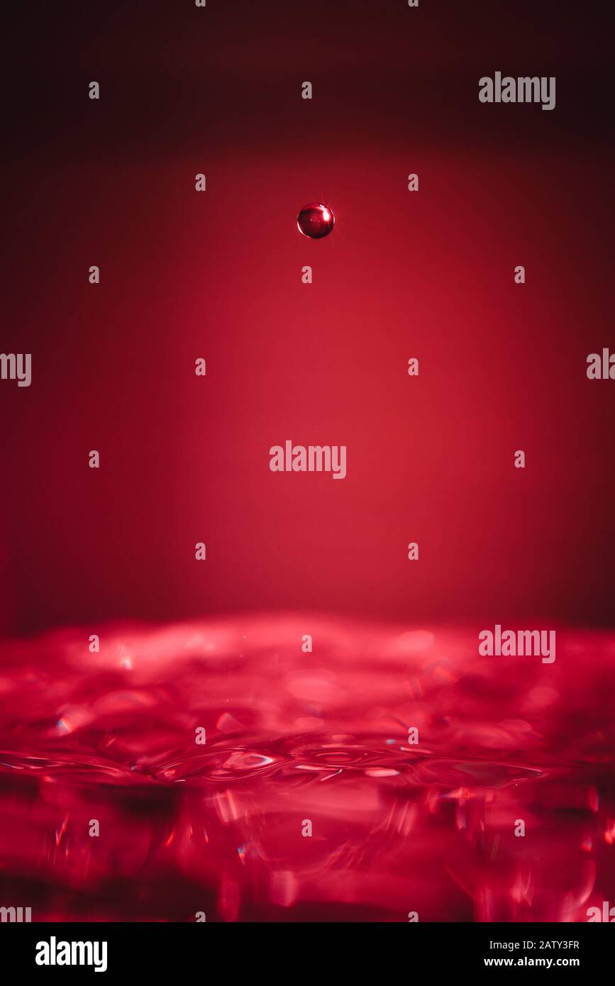 Water drop midair above bowl of water red background Stock Photo
