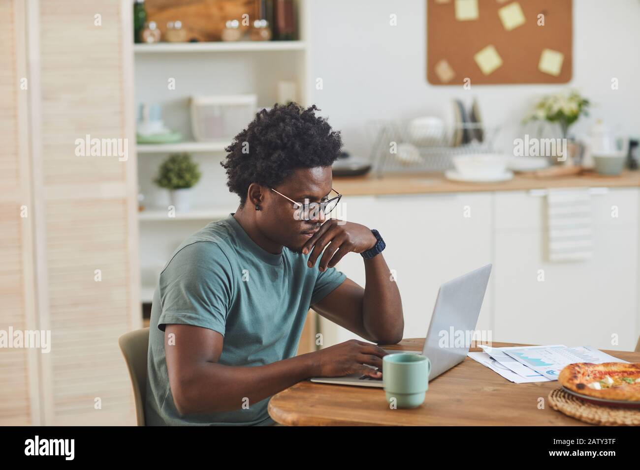 African young man sitting at the table and working on laptop in the kitchen at home Stock Photo