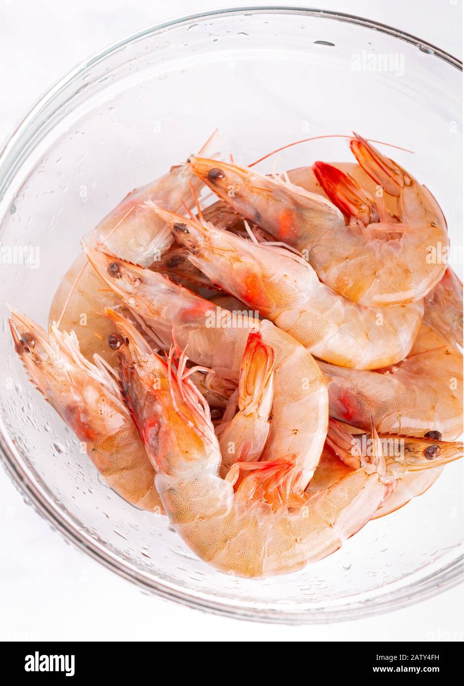 Fresh, raw, unpeeled shrimp in a clear glass bowl with copy space Stock Photo