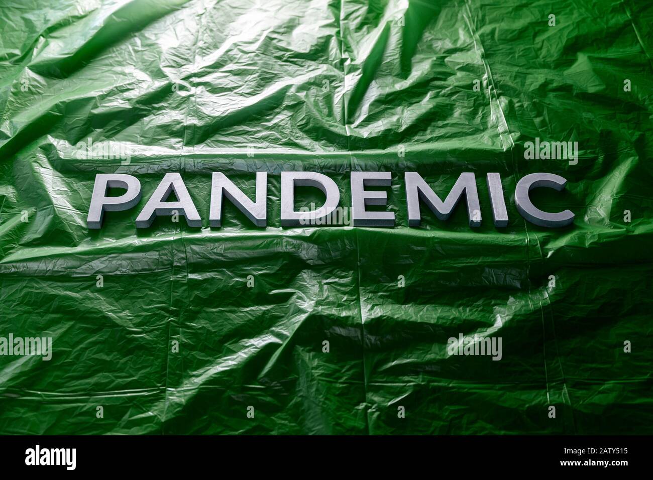 The word pandemic laid with silver letters on crumpled green plastic film background Slanted centered with dramatic cold light. Stock Photo