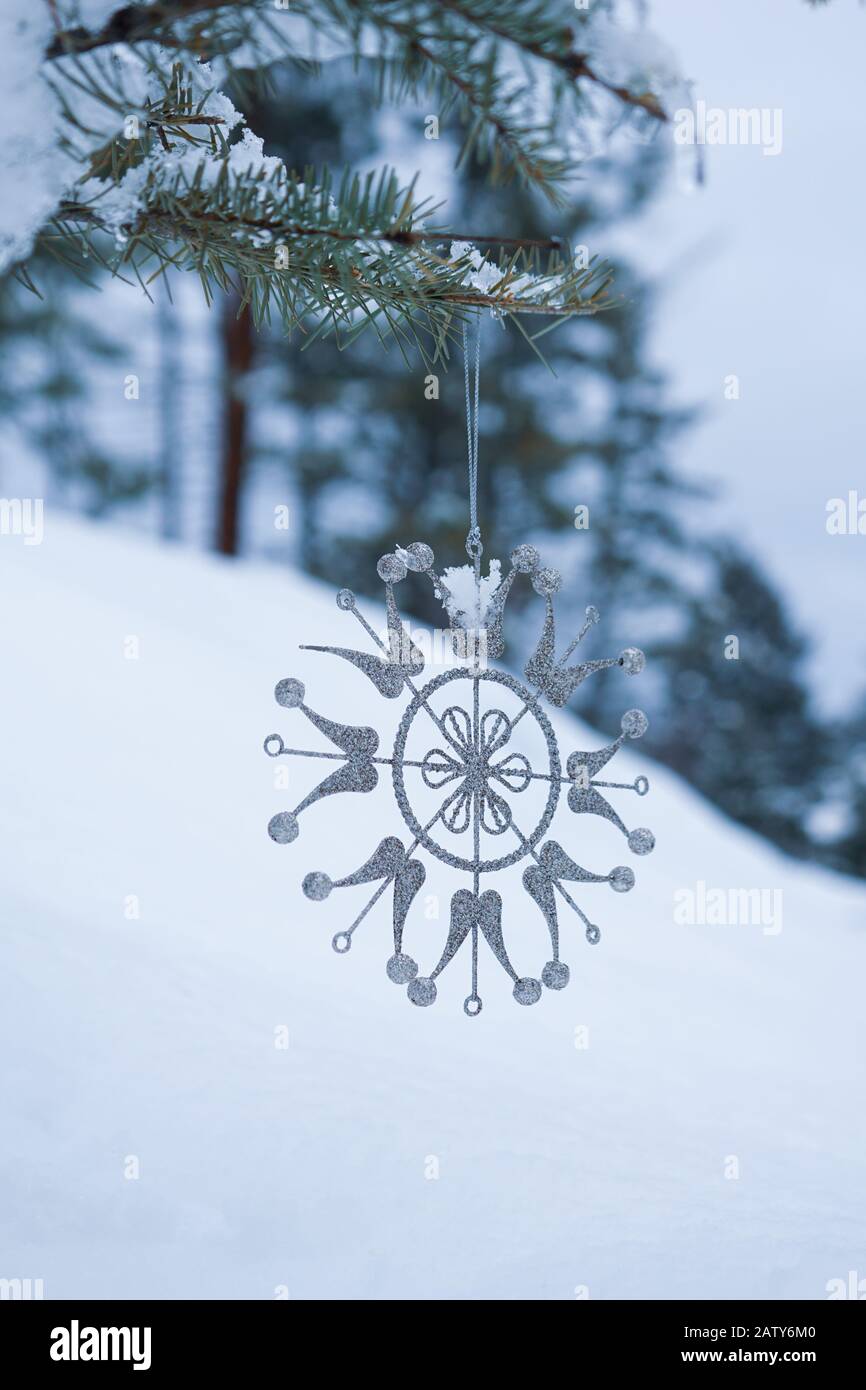 Snow flake shaped ornament hangs on the snow covered branch of an evergreen tree Stock Photo