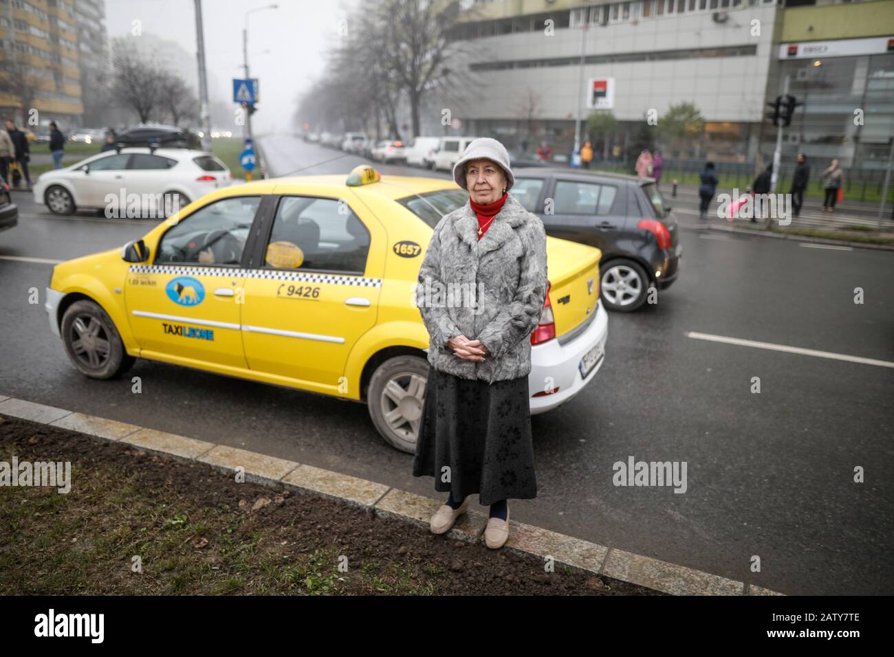 Bucharest, Romania - December 20, 2019: Shallow depth of field image with a senior woman standing on a concrete ledge on a crossroad in downtown Bucha Stock Photo
