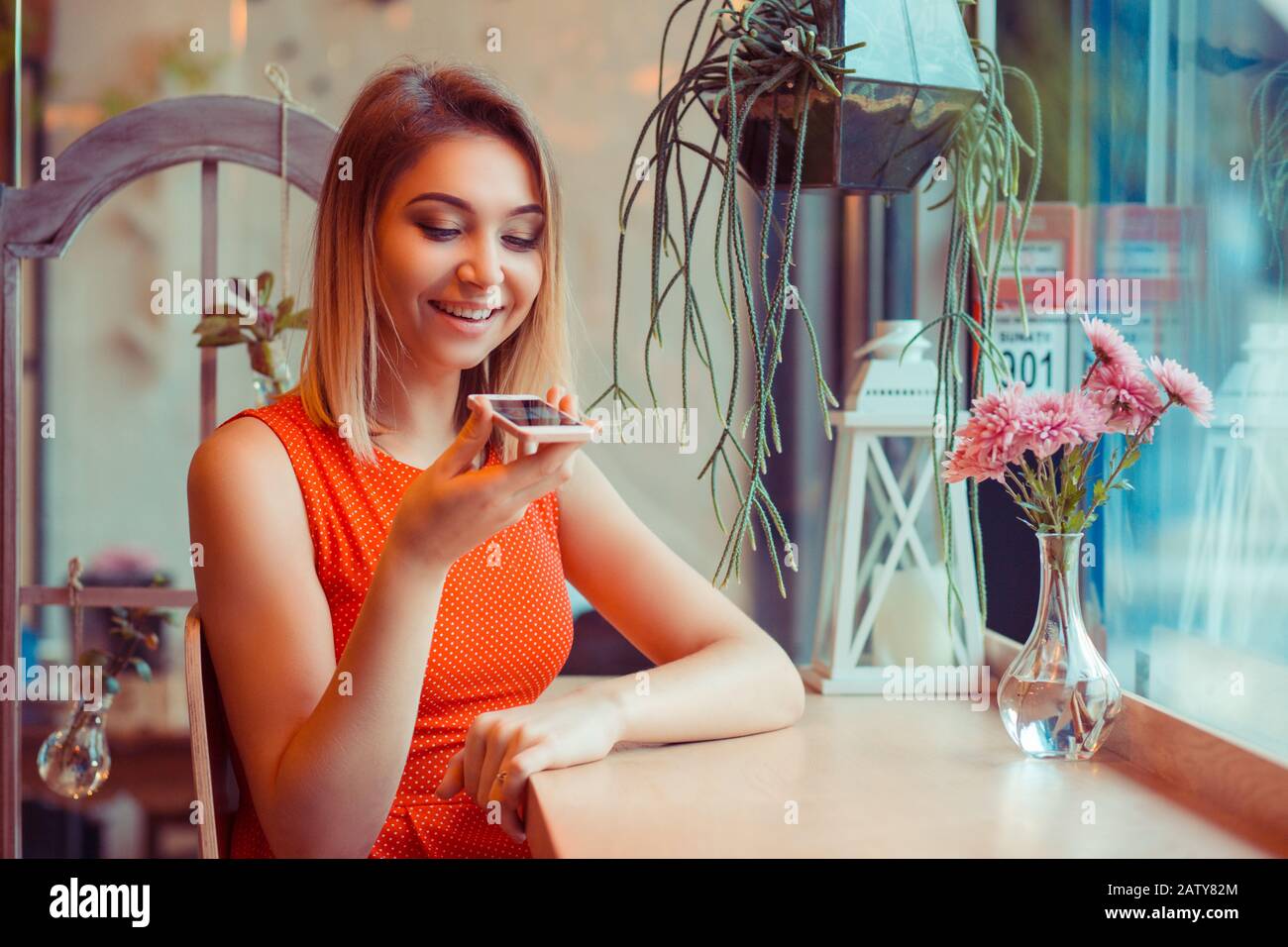 Portrait of a girl using the voice recognition of the phone and looking at cell phone near a window of a house or coffee shop Stock Photo