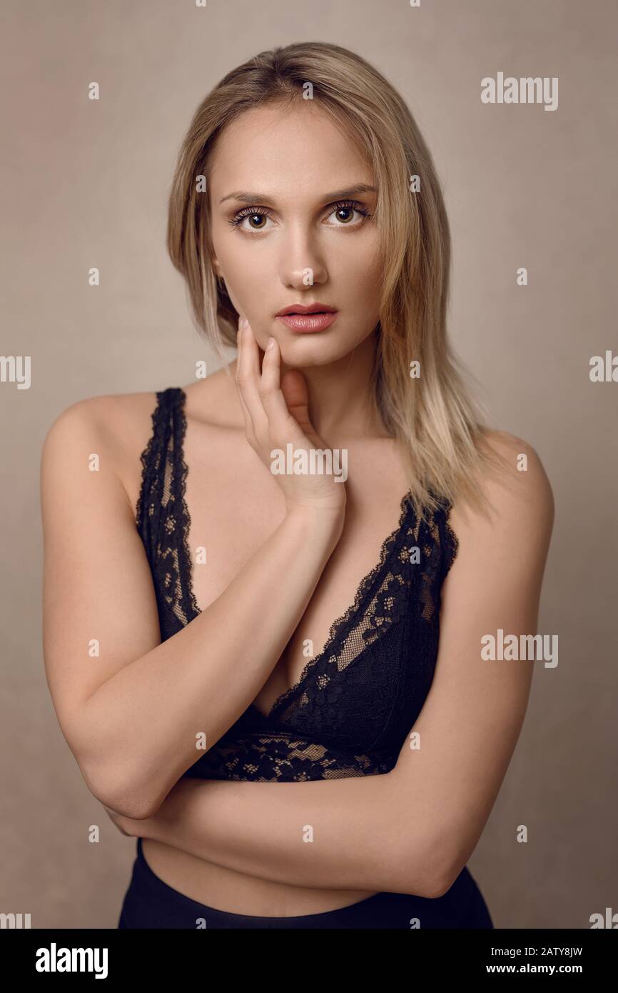 Attractive young blond woman in sexy black lacy lingerie staring intently at the camera with her hand gracefully raised to her chin Stock Photo