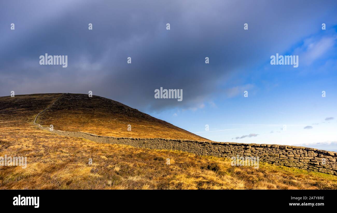 Mourn Wall on the bank of Slieve Donard mountain with blue sky, white clouds and sunlight. Mourne Mountains range in Northern Ireland Stock Photo