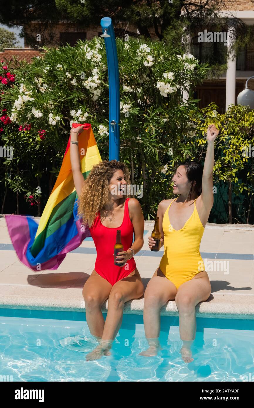 Two Laughing Beautiful Women Raise Their Fists And Wave A Rainbow Flag While Sitting At The Poolside Gay And Diversity Concept Stock Photo Alamy