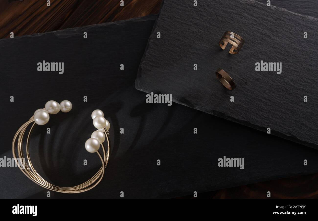 Golden and pearl bracelet and golden rings on black stone plates on wooden background Stock Photo