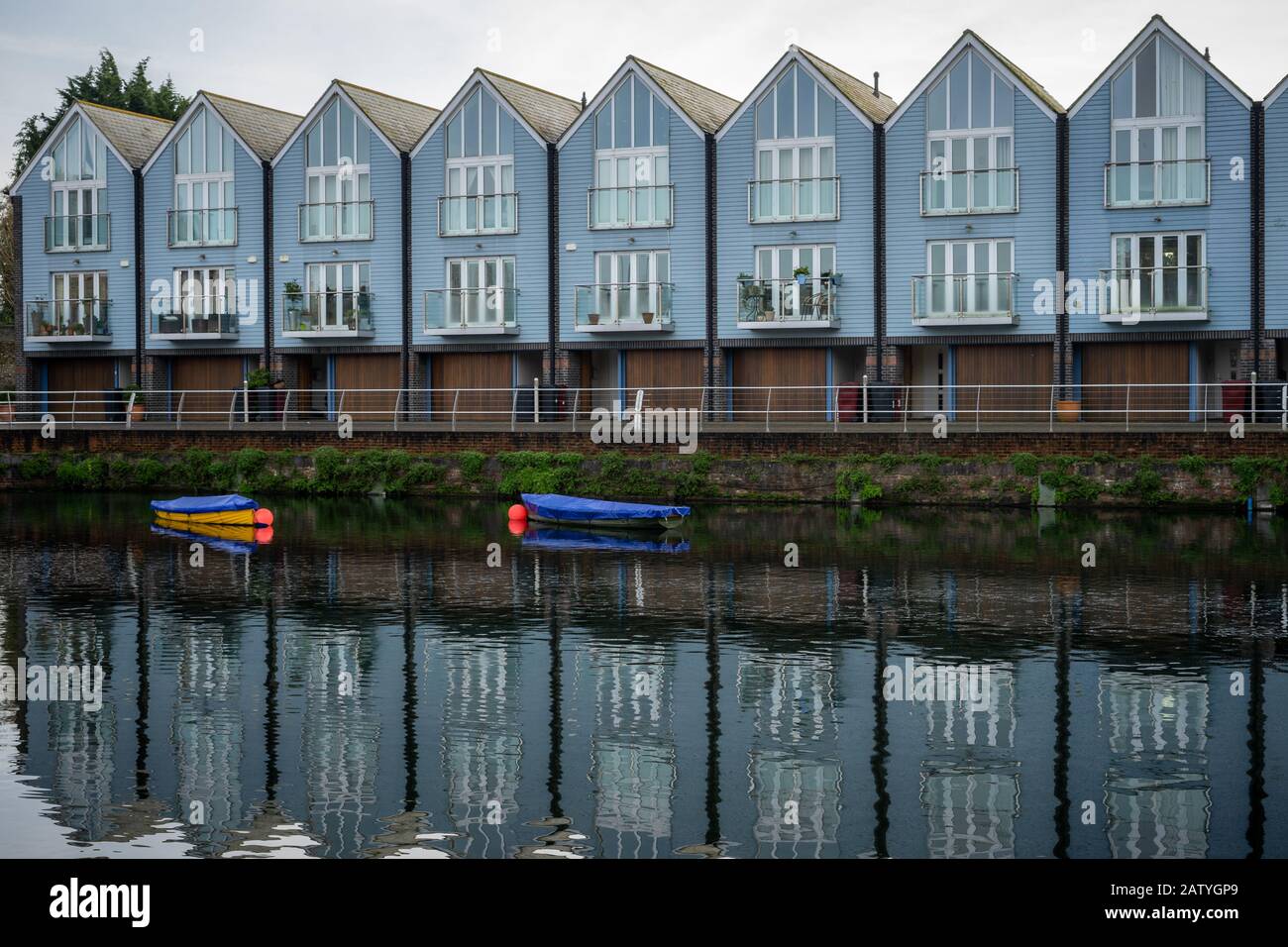 A row of modern townhouses overlooking a river reflecting on the water Chichester canal, west Sussex UK Stock Photo