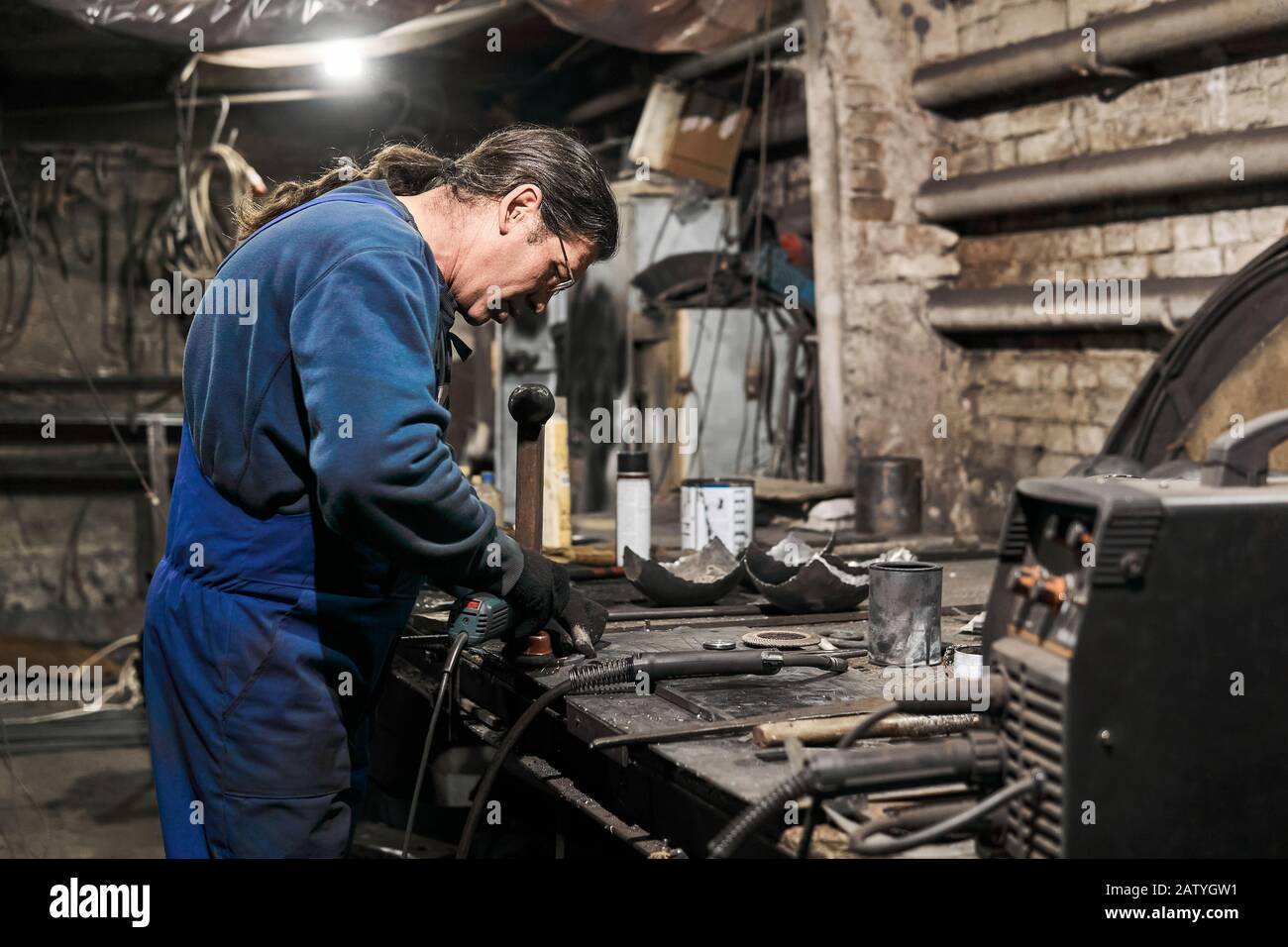 aged male locksmith processes the workpiece using an angle grinder Stock Photo