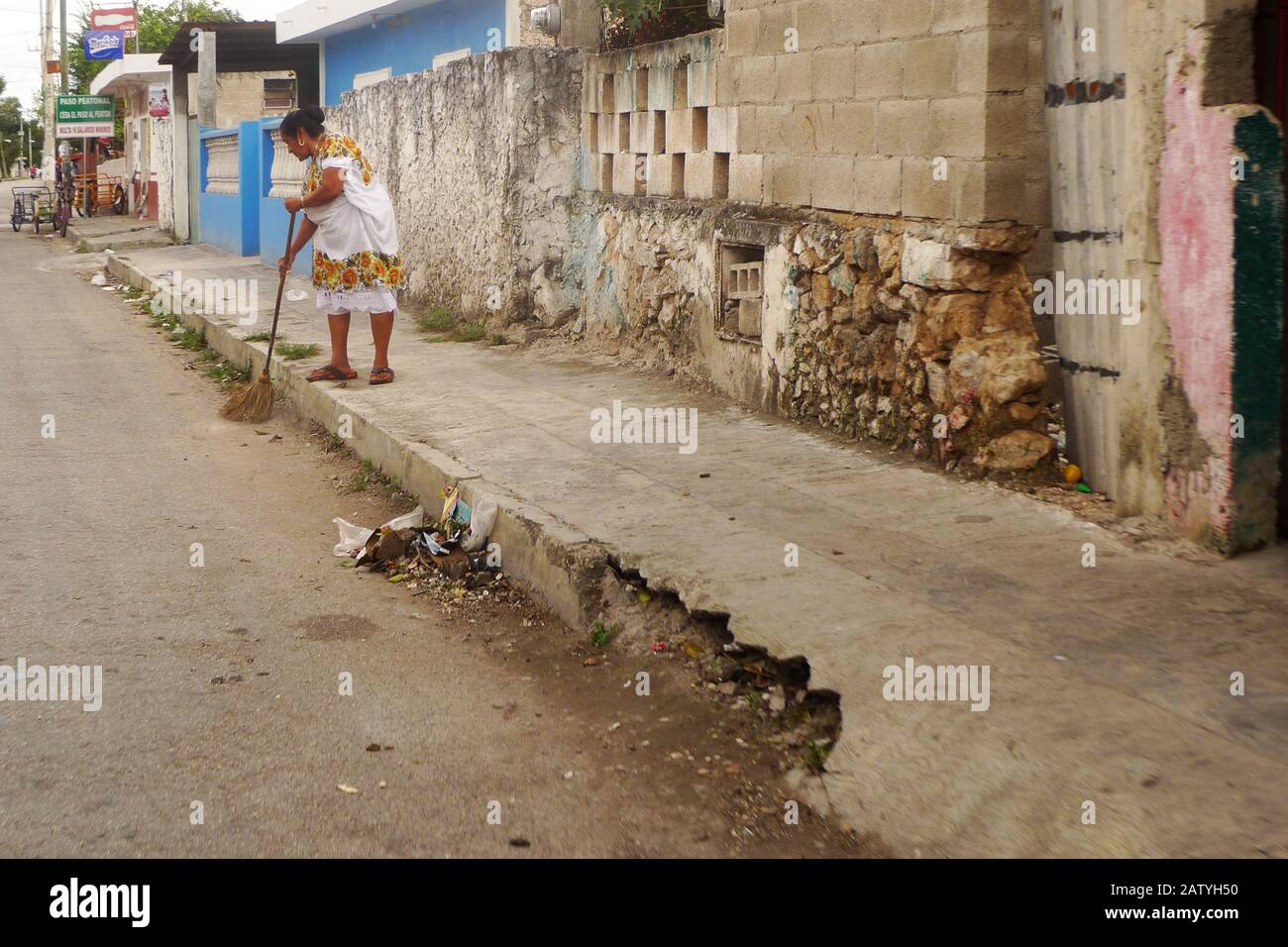 A woman in a huipil sweeps a street in Hunucma, Yucatan, Mexico. Stock Photo