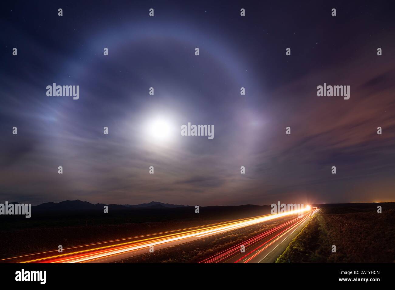 A moon halo in the night sky above car light trails on Interstate 10 near Tucson, Arizona Stock Photo