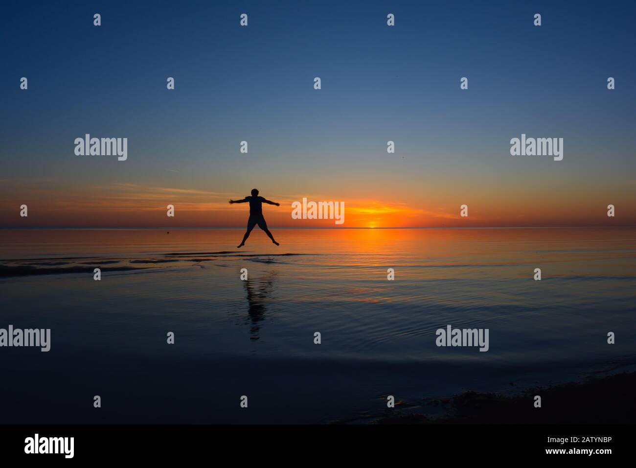 happy person jumps on the beach, visible siloutte on sunset, scenic beach with beautiful light Stock Photo