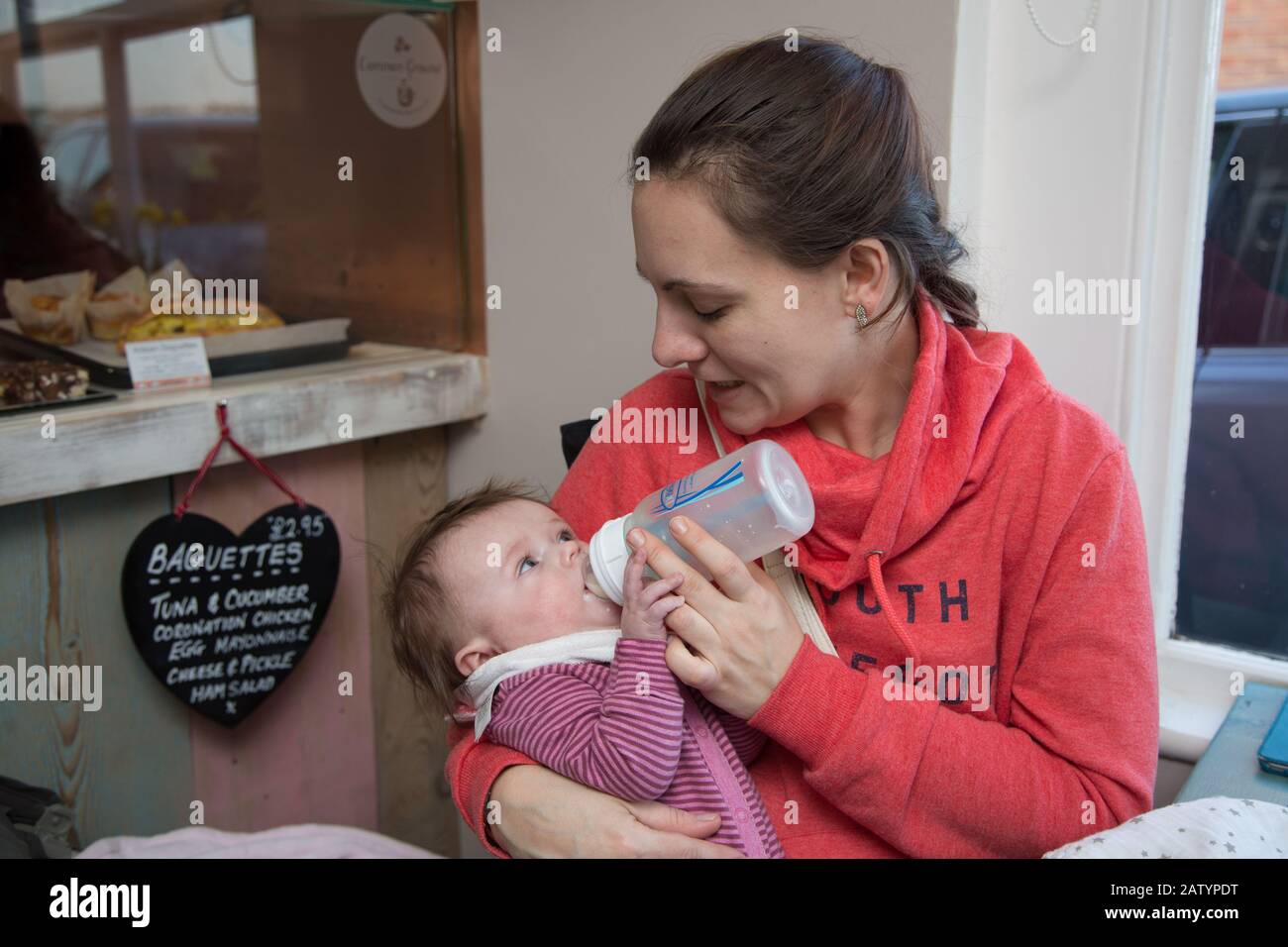 A young mum bottle feeding her 4 month old baby in a cafe, UK Stock Photo