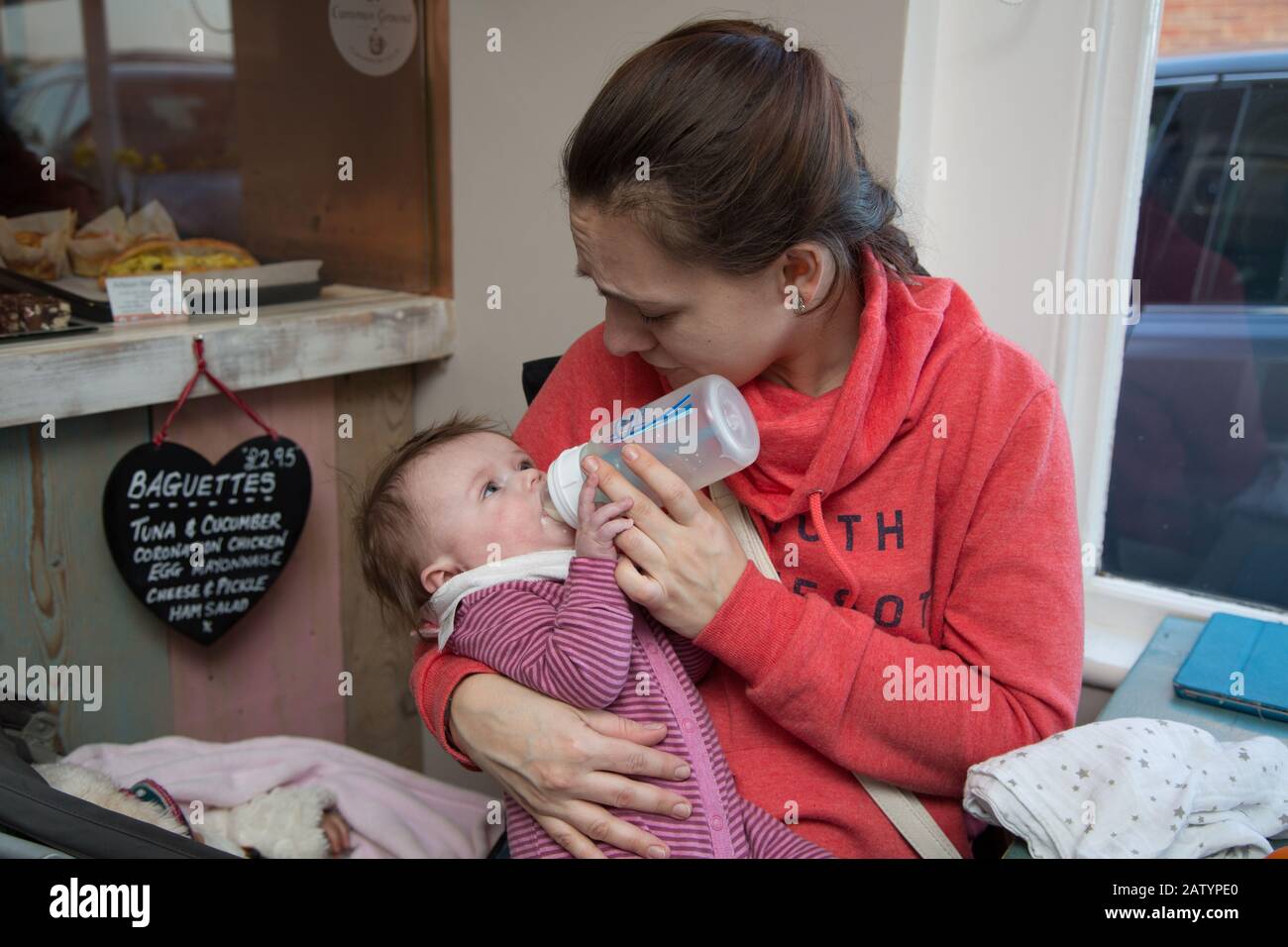 A young mum bottle feeding her 4 month old baby in a cafe, UK Stock Photo